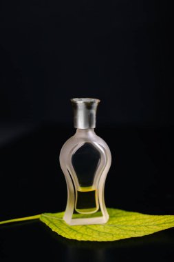 Siyah arka planda parfümlü cam şişe. Yeşil yaprak. Tazelik aromaları