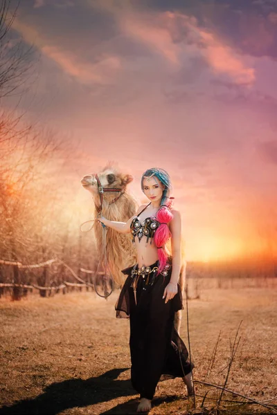 Beautiful girl with multi-colored braids in oriental clothes. Princess with a camel at sunset. in desert — Stock Photo, Image
