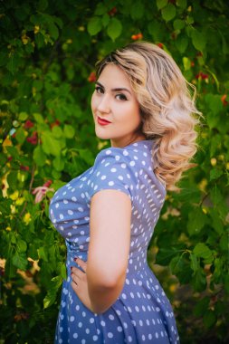 Kırmızı dudaklı ve parktaki ağaçların arka planında bezelye desenli elbisesi olan bir kız. Kırmızı elmaların arkaplanındaki pin-up modeli.