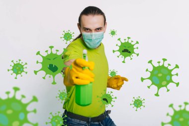 Yeşil tişörtlü ve tıbbi maskeli bir adam elinde beyaz arka planda antiseptik olan bir kurşun tutuyordu. Adamın biri koronavirüsü öldürüyor. Odayı dezenfekte eder