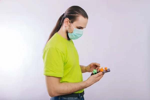 Ένας τύπος με πράσινο μπλουζάκι κρατάει ένα smartphone με έναν κορωναϊό στην οθόνη. Βρωμερό τηλέφωνο. Προσωπική υγιεινή — Φωτογραφία Αρχείου