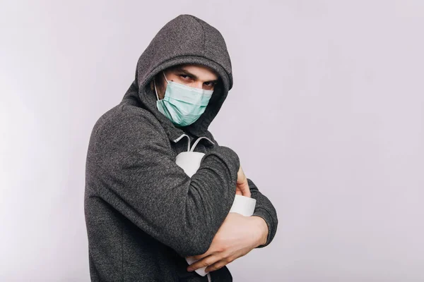 회색 운동복을 입고 화장지를 들고 하얀 배경에 서 있는 한 남자가 있습니다. 코로나 바이러스 격리 기간의 흥분이요. 의료용 마스크를 쓴 남자의 몸 속에 있는 로타바이러스. — 스톡 사진