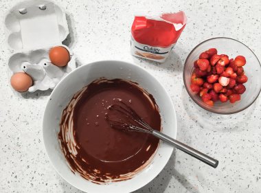 Çikolatalı pasta hazırlıyorum porselen beyaz bir kasede erimiş çikolata çırpılmış yumurta, şeker ve dilimlenmiş çilek.
