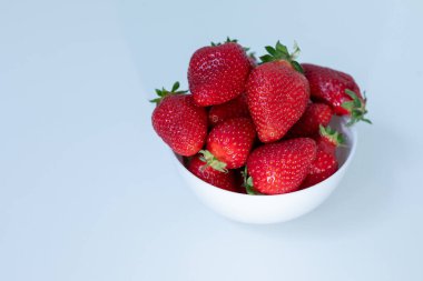 Beyaz arka planda beyaz seramik bir bardakta çilekler.