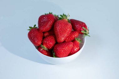 Beyaz arka planda beyaz seramik bir bardakta çilekler.