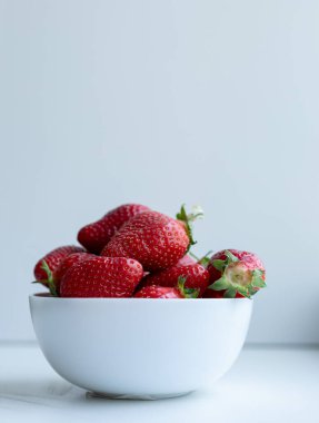 Beyaz arka planda beyaz seramik bir bardakta çilekler.