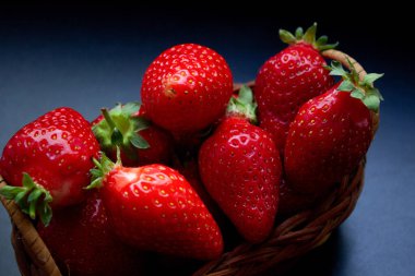 Siyah masanın üzerinde örülmüş bir sepetin içinde çilekler.