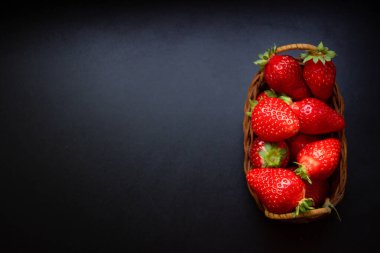 Siyah masanın üzerinde örülmüş bir sepetin içinde çilekler.