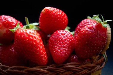 Siyah masanın üzerinde örülmüş bir sepetin içinde çilekler.