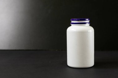 Siyah arka planda haplarla dolu beyaz plastik bir kavanoz.