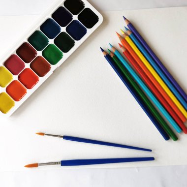 suluboya boyalar, renkli kalemler ve beyaz kağıt üzerinde fırçalar çizmeye hazır.