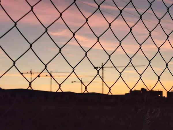 日没の背景と建設クレーンのフェンスネット — ストック写真