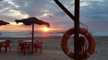 Akdeniz kıyısındaki kumsalda gün batımında bir kafeteryada.