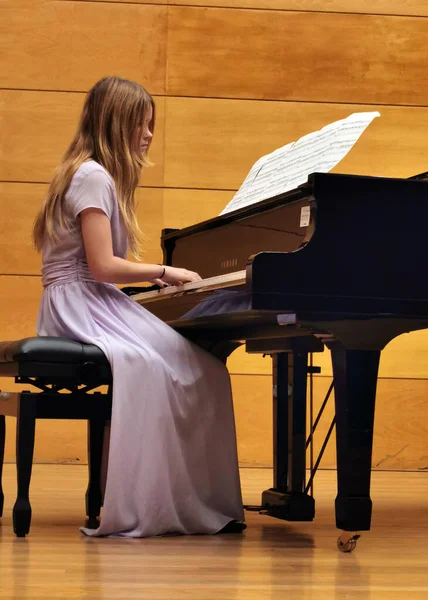 young pianist in a lilac dress at the piano in a concert hall