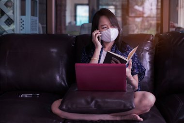 Evde dizüstü bilgisayarda çalışan kadın 2019-nCov, covid 19 ya da corona virüsünü korumak için tıbbi maske takıyor..