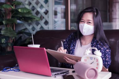 Evde dizüstü bilgisayarda çalışan kadın 2019-nCov, covid 19 ya da corona virüsünü korumak için tıbbi maske takıyor..