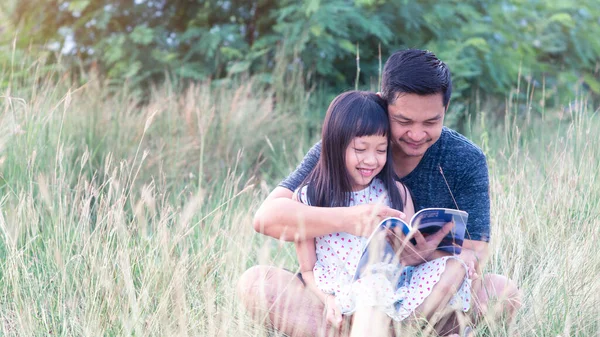 Asyalı Bir Baba Çimenlerde Oturuyor Küçük Kızı Üzerine Oturmuş Kitap — Stok fotoğraf