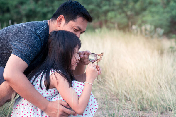 Happy asian family father and daughter exploring nature with magnifying glass.