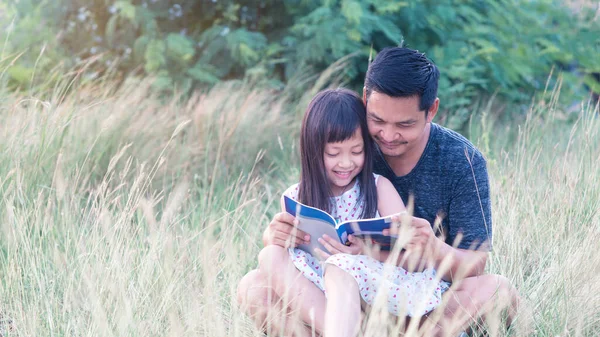 Asyalı Bir Baba Çimenlerde Oturuyor Küçük Kızı Üzerine Oturmuş Kitap — Stok fotoğraf