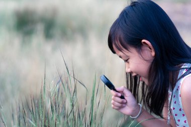 Mutlu Asyalı kız büyüteçle doğayı keşfediyor..