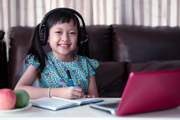Sevimli Asyalı küçük kız evde online ders çalışıyor, karantina sırasında sosyal uzaklık, online eğitim konsepti