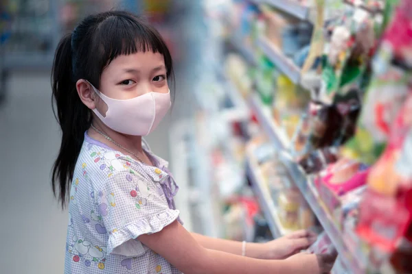 Shopping Concept with asian kids during virus outbreak. Child wearing surgical face mask buying fruit in supermarket in coronavirus pandemic. Little boy buy fresh vegetable in grocery store. Covid-19 epidemic.
