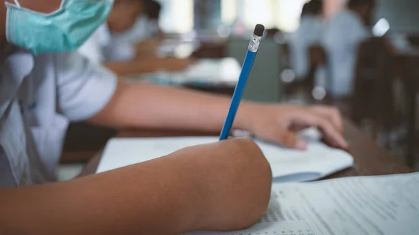 Corona virüsünü veya covid-19 'u korumak için maske takan öğrenciler ve sınıfta stres altında muayene oluyorlar. 16: 9 stili.