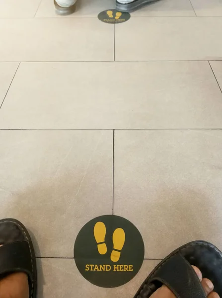 Stand here foot sign or symbol on the floor with the people is waiter , Social distancing concept.