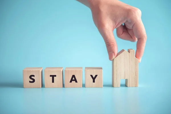 Woman hand holding wood cube with word stay home.