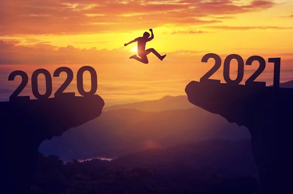2020 ve 2021 yılları arasında gün batımı geçmişiyle siluet adam sıçrama, Başarı yeni yıl konsepti.