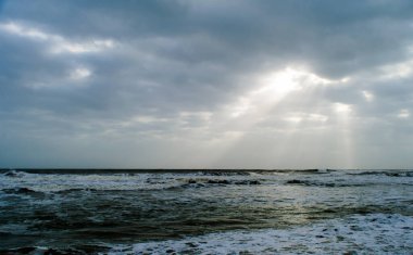 Güneş ışığı bulutların arasından denize akıyor. Somnath tapınağı Gujarat Hindistan 'ın plajından görünüyor.
