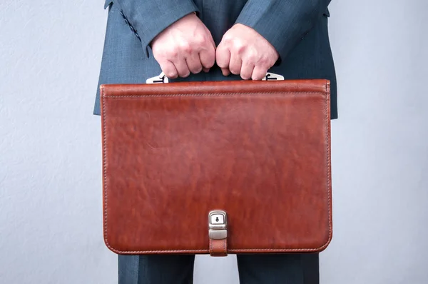 Kahverengi bir evrak çantası tutan iki elli bir adam.