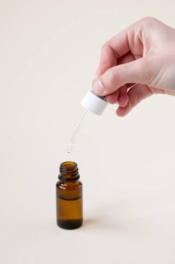 Siyah bir cam şişenin üzerinde pipeti tutan el, burun damlası, göz damlası