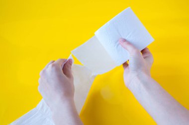 Eller sarı arka plandaki beyaz tuvalet kağıdından bir parça koparır.