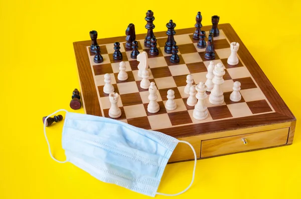 Board game, wooden chess and a medical mask on a yellow background, the concept of leisure during the quarantine