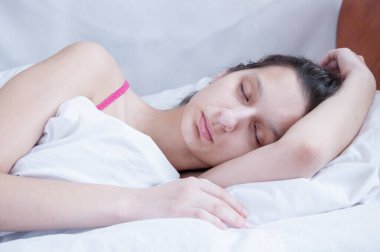 Esmer kız beyaz yastıkta yatağında uyuyor.
