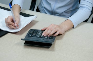 Ofis, esmer muhasebeci kız masasında hesap makinesiyle çalışıyor.