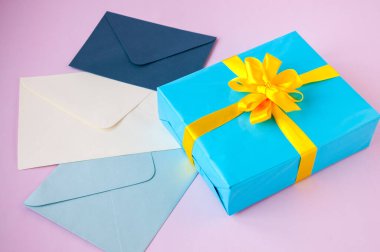 Mavi bir kutuda, sarı bir fiyonk ve pembe bir arka planda zarflar.