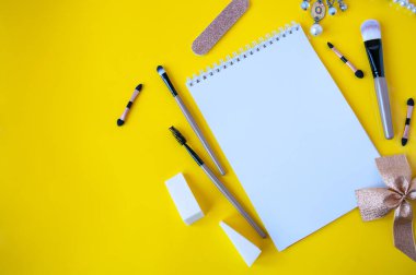 Sarı arka planda not defteri ve kozmetik fırçalar