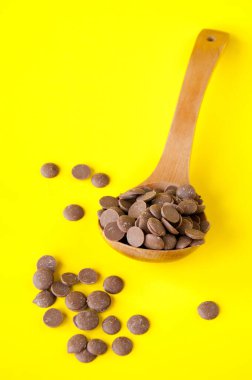 Sarı arka planda büyük bir tahta kaşıkta süt çikolata damlaları