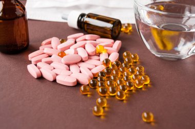 Tıbbi hayat: tabletler, balık yağı, tıbbi maske, kahverengi arka planda bir bardak su ve ilaç.