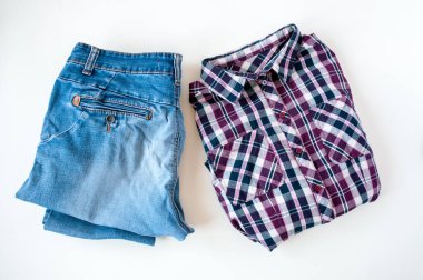 Giysiler, katlanmış ekose gömlek ve açık arkaplanda kot pantolon.