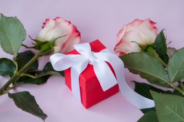İki açık sarı-kırmızı gül ve kırmızı bir kutuda bir hediye üzerinde pembe bir kurdele