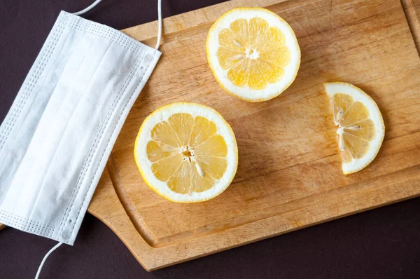 On a wooden cutting Board, a medical mask and pieces of lemon on a brown background, top view
