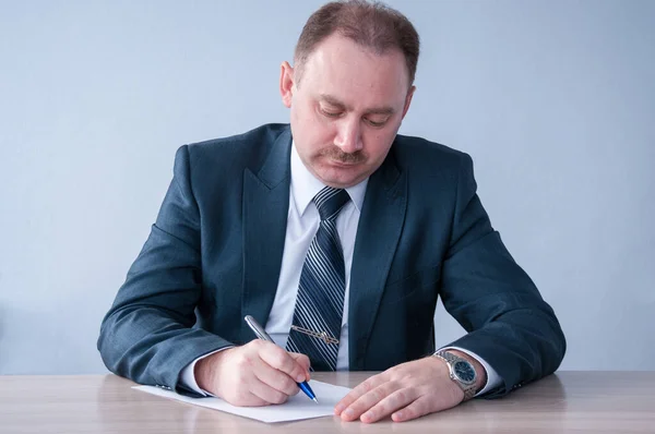 Takım elbiseli bir adam kağıda yazı yazıyor.