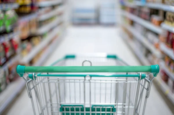 Blurred effect in the Supermarket aisle with empty silver and green shopping trolley,  Shopper choosing the food in supermarket Panic buyer for hoarding food, Coronavirus Covid-19 concept.