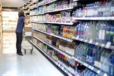 Coronavirus (COVID-19) salgını için yiyecek stoklamaya hazırlanmak üzere süpermarket koridorunda yiyecek düzenleyen kadın işveren. 