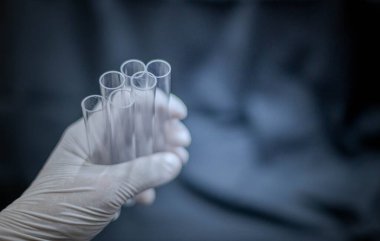 Bilimadamları test tüpünü tutuyor ve eldiven takıyor. Laboratuar odasındaki bilim deneyine hazırlanıyor.. 