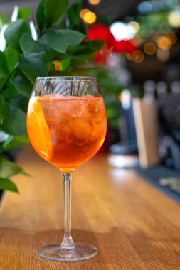 Aperol alkollü bir kokteyl. Turuncu. Buz küplü soğuk içecek. Bardak barın üstünde. Arka planda yeşil. Arka plan bulanık. Restoranlar, kafeler ve barlar için menü.