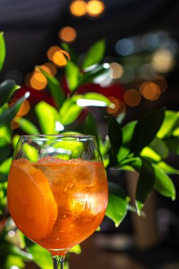 Aperol alkollü bir kokteyl. Turuncu. Buz küplü soğuk içecek. Bardak barın üstünde. Arka planda yeşil. Arka plan bulanık. Restoranlar, kafeler ve barlar için menü.